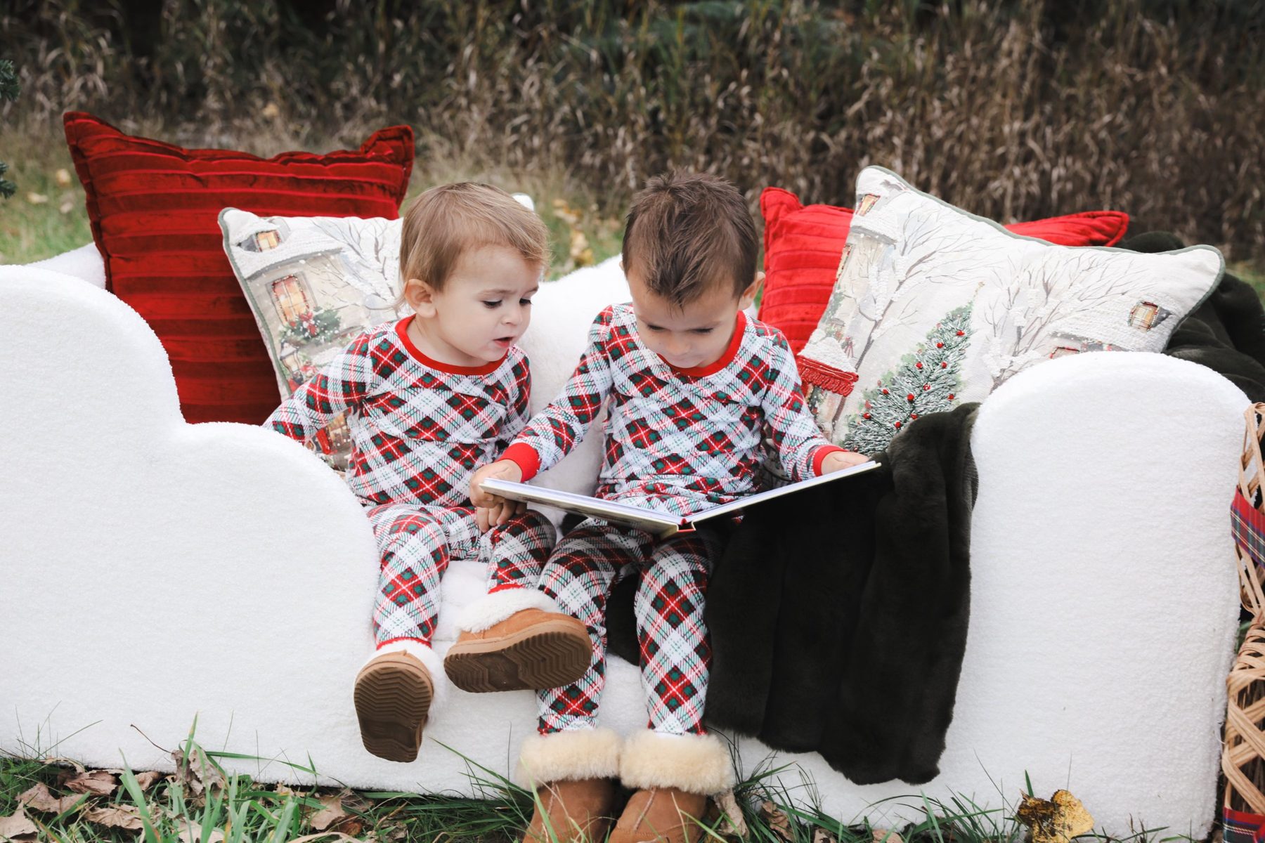 Two toddlers in plaid pajamas reading a book together
