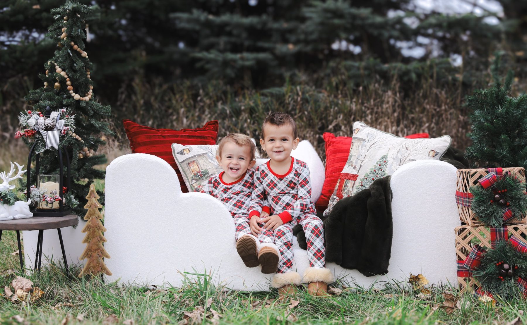 Two laughing brothers on a white sofa with Christmas trees