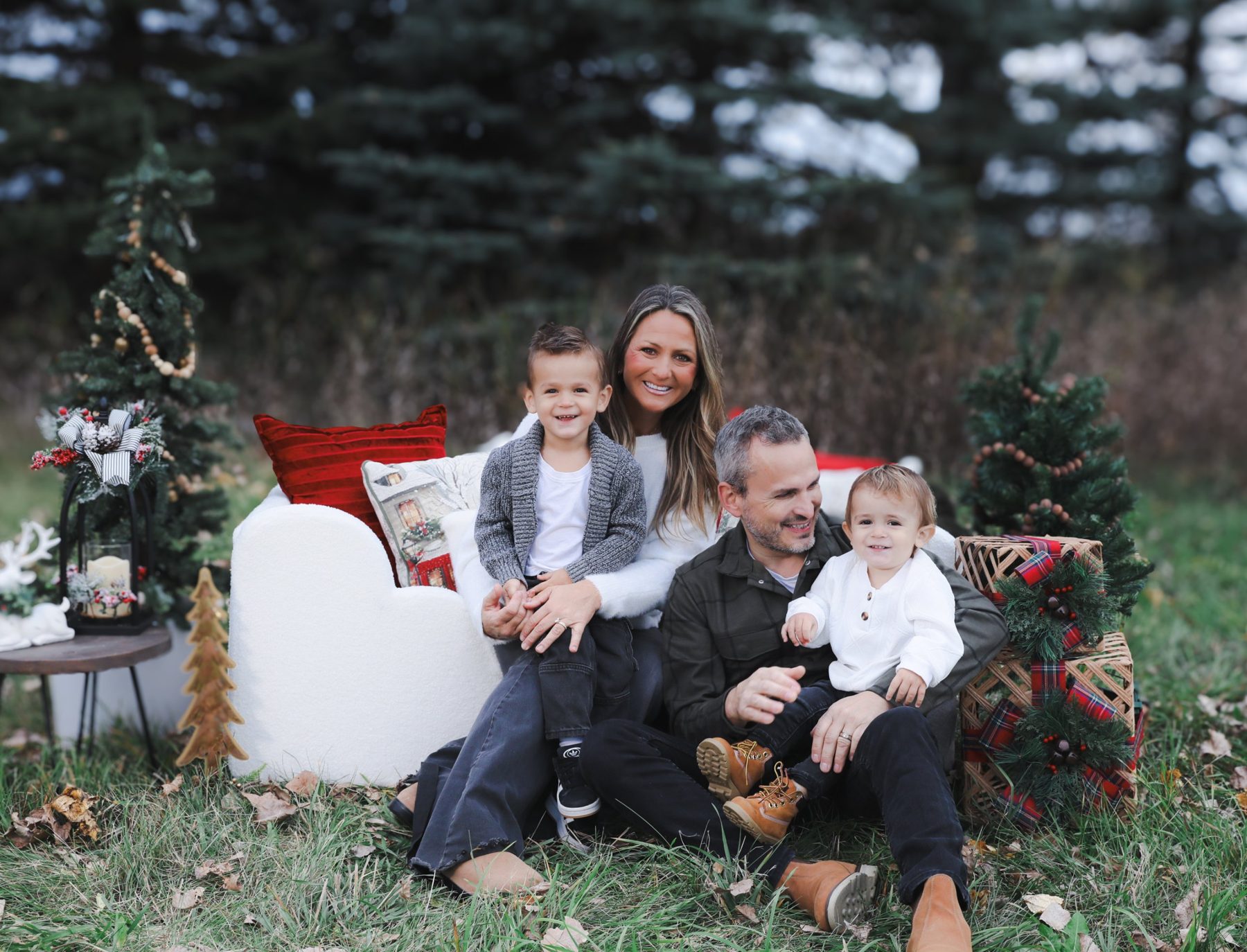Family of four on a white sofa in front of evergreens, Christmas mini session