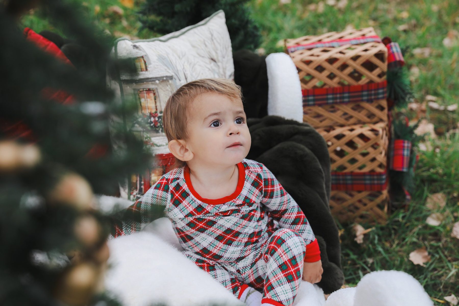 Toddler in plaid pajamas looking up past a Christmas tree