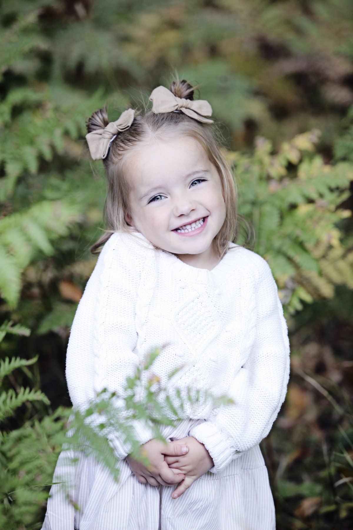 Little girl in a white dress laughing among ferns